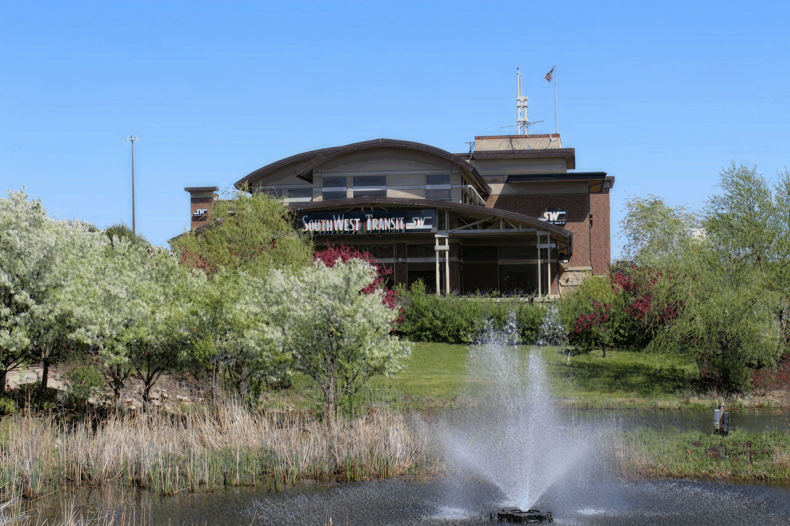 Southwest Transit station building surrounded by trees and landscaping, with a water fountain spraying in a pond in the foreground